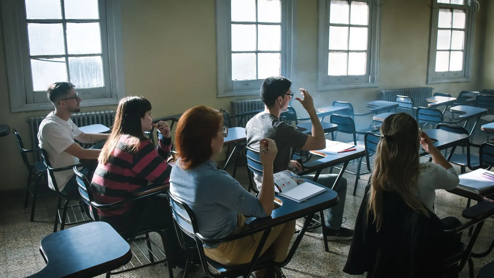 Grupo de adultos atendiendo una clase en una sala con pupitres y luz natural