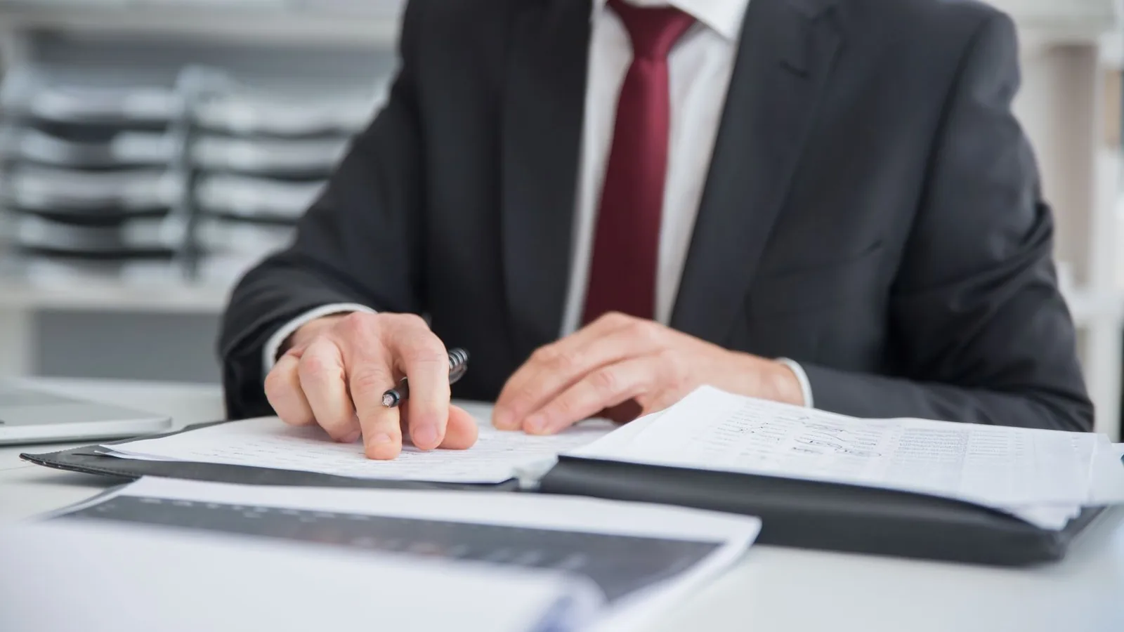Persona de traje revisando documentos con un lápiz sobre un escritorio de oficina